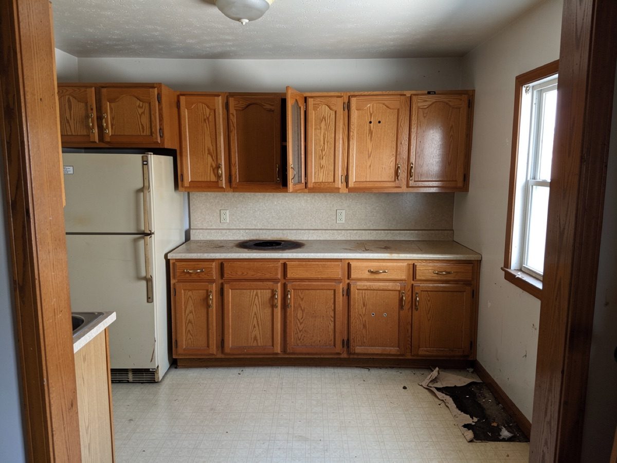 A tired 1990s oak kitchen with a damaged floor